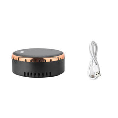 A round black and rose gold electronic device shown next to a white USB charging cable on a plain white background.