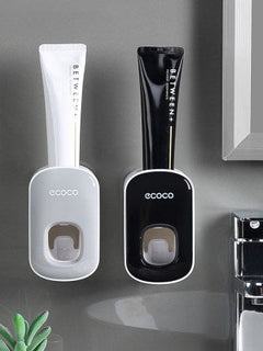 Two toothpaste dispensers, one white and one black, with 'ecoco' branding on a gray surface.