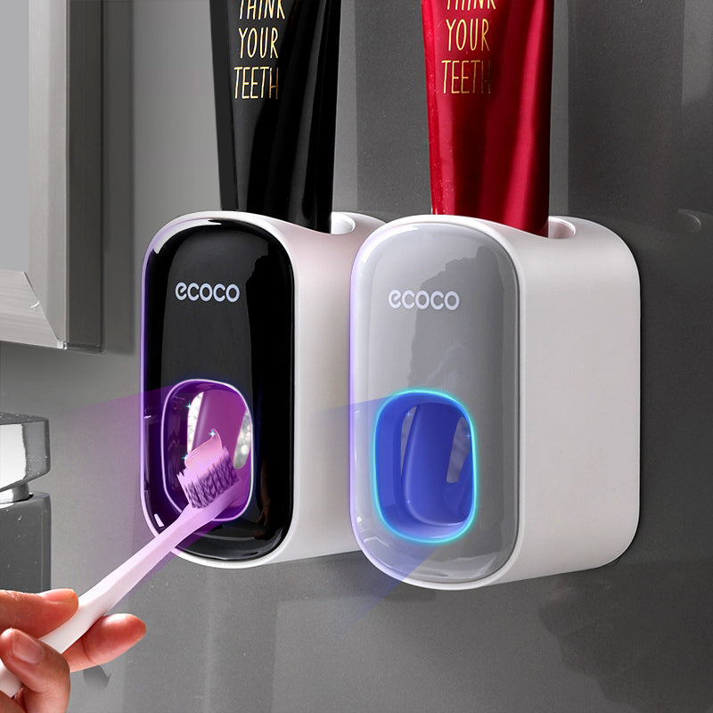 Two ecoco toothbrush holders with a hand holding a purple toothbrush against a gray background.