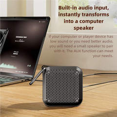 A small black audio speaker sits on a wooden desk next to a laptop, with promotional text explaining built-in audio input and AUX connection.