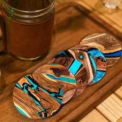 Wooden coasters with blue resin on a wooden surface next to a glass mug.