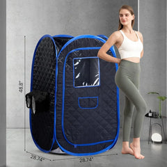A portable pop-up sauna tent with a woman standing next to it in a gray room. The tent is dark gray with bright blue trim and a clear window on the front.