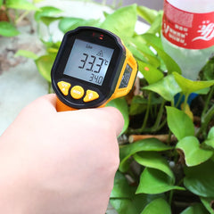 Digital thermometer held by a hand with plants in the background