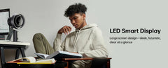 A man in a light gray hoodie sits at a desk reading a book, with a desk lamp on the left and promotional text on the right reading 'LED Smart Display' and 'Large screen design—sleek, futuristic, clear at a glance.'.