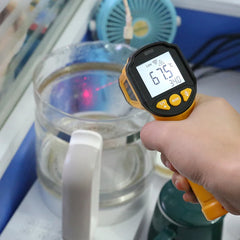 Digital thermometer measuring temperature of a glass container with water and a white object inside.