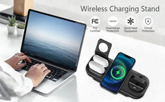 A black wireless charging stand shown on a white desk, with a smartphone placed on one charging pad and two white earbuds in another pad. A person's hands and arm are visible using a laptop in the background, and text highlights FCC certification and protection features.
