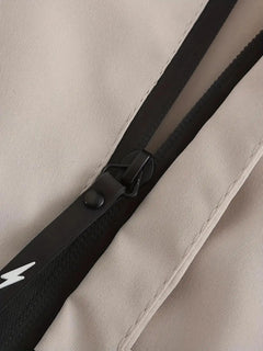 Close-up of a beige fabric item with a black zipper and black trim, showing a small white lightning-bolt logo on the black tab.