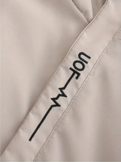 Close-up of a light beige or off-white fabric surface with a black printed or embroidered vertical graphic and partial text reading "uof".