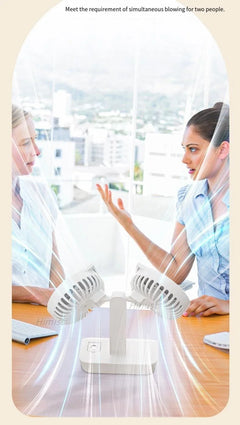Two women sitting at a desk with a white office fan blowing air towards them.