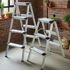 Two silver aluminum step ladders with black rubberized tips and joints, displayed in a home environment with a brick wall, potted plants, and a concrete floor.
