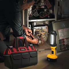 Person working on an appliance with a tool bag and flashlight nearby