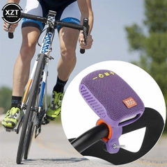 A purple portable speaker mounted on a bicycle handlebar, shown with a close-up inset of the speaker attached and a cyclist riding in the background.
