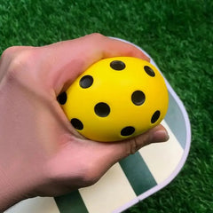 Hand holding a yellow ball with black dots against a green grass background