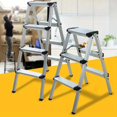 Two silver aluminum step ladders with black rubberized pads on the steps and joints, shown in a kitchen setting with a blurred background of a person working high up.