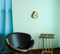 Modern black chair and wooden side table against a light green wall with a clock.