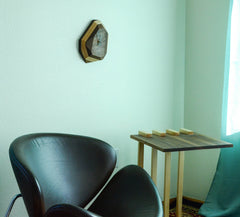 Modern interior with a black chair, wooden side table, and wall clock on a light green wall.